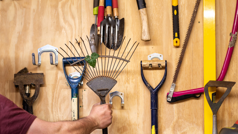 A variety of garden tools hang on a wall.