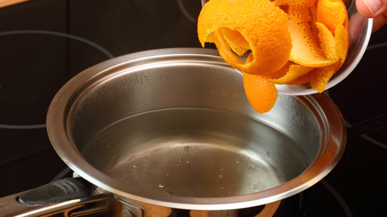 A person adds orange peels to a boiling pot of water.