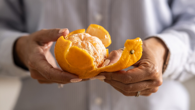 A woman peels an orange in her hands.