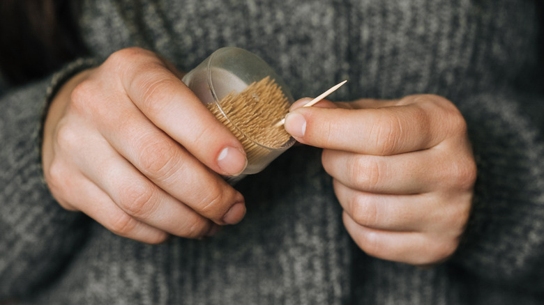 Woman pulls out a single toothpick from a container.