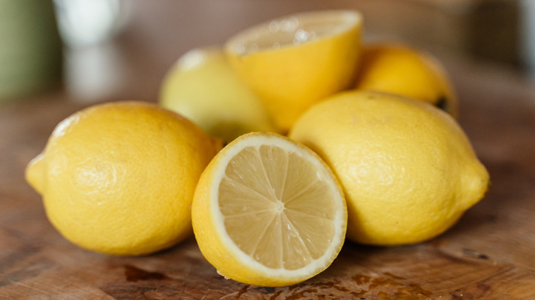 Whole and cut lemons sit on a wooden cutting board