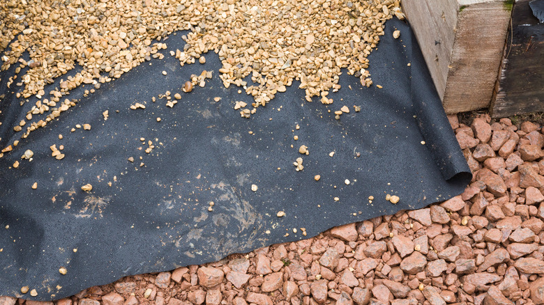 Gravel lays on top of roll plastic landscape cloth.