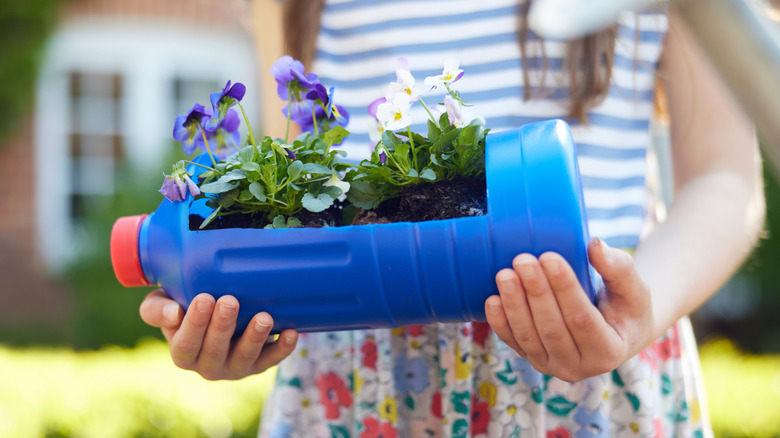 A girl holds a plastic bottle turned into a planter for flowers.