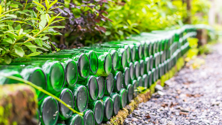Green glass bottles stacked on top of one another make a garden wall.