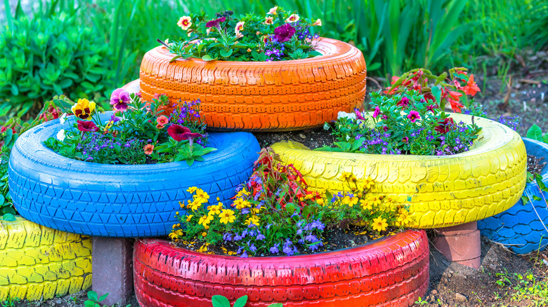 Colorful reused tires repurposed as planters hold flowers.