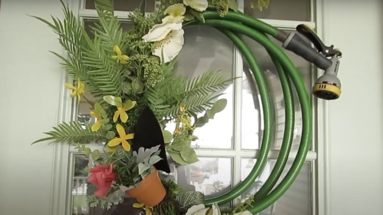A wreath made out of a garden hose and fake flowers hangs on a door.