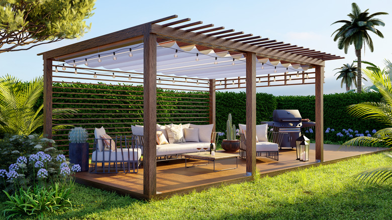 A wooden pergola with retractable shade stands over seating area in the garden.