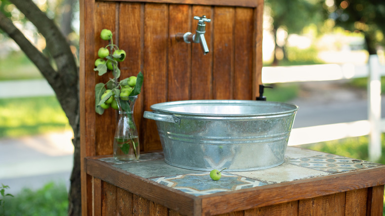 An outdoor sink sits near tree, made of old wash pan and garden hose nozzle.