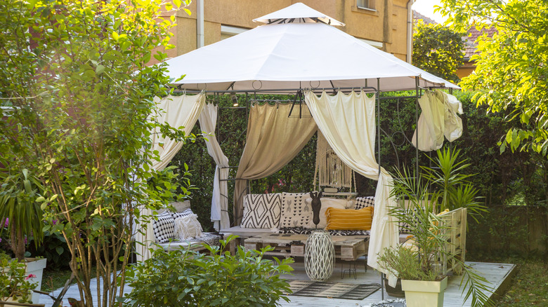A gazebo made of fabric shelters a seating area in a yard.