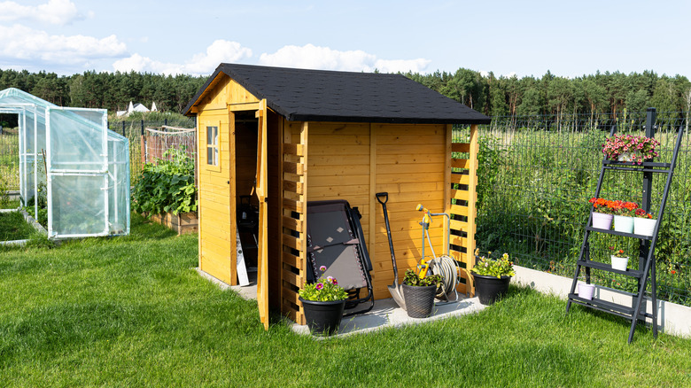 A garden shed with door open sits near a fence.