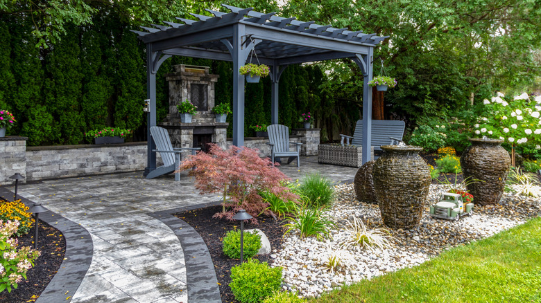 Stone path leads to seating area and fireplace offset by a gray pergola.