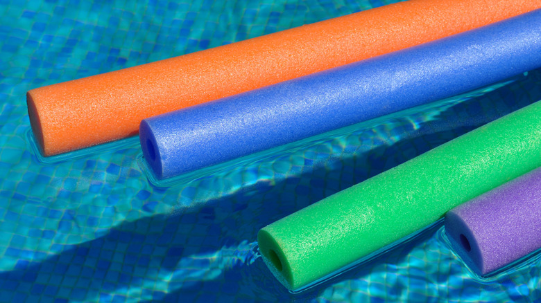 Colorful pool noodles float in a pool.