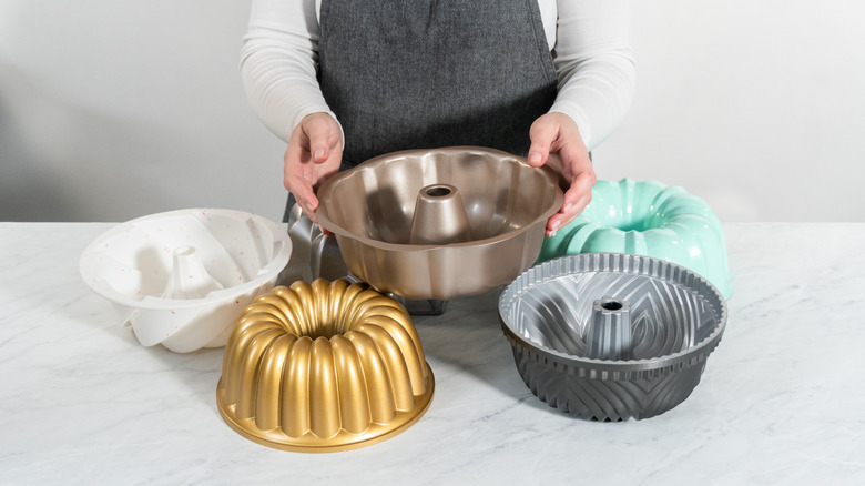 A person has a variety  of different Bundt pans on a table in front of them.