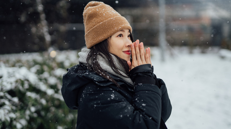 A young woman enjoys a snowy day with a hat and coat on.