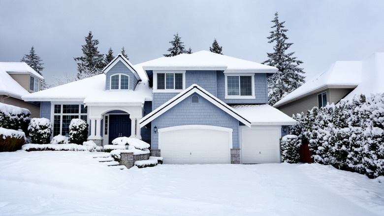 A blue suburban home is blanketed in snow from a recent storm.