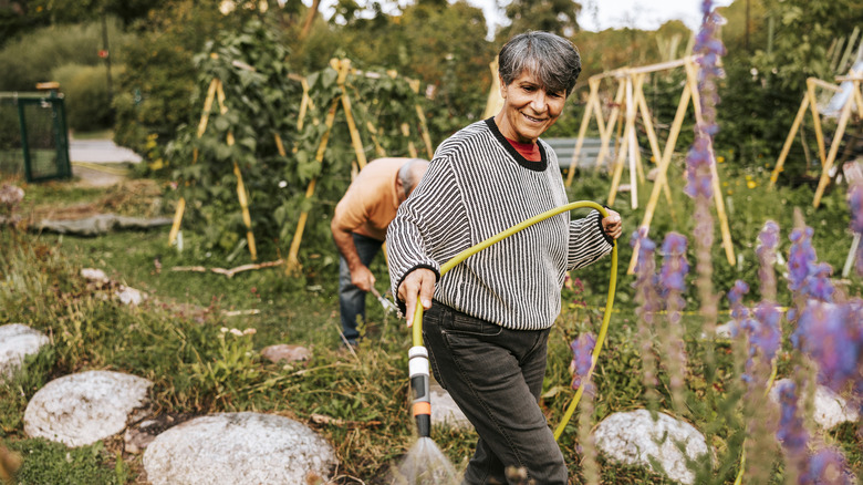 A woman holds a yellow garden hose as she waters the garden.