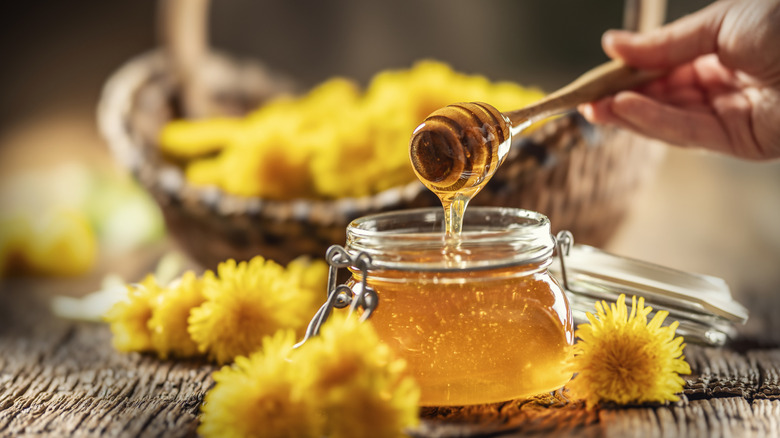 A woman holding a dipper over a pot of honey that's surrounded by dandelions
