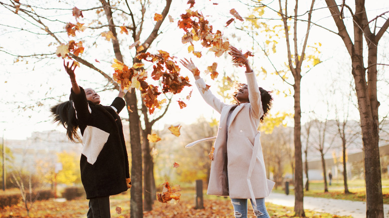 Two friends throw leaves in the air.